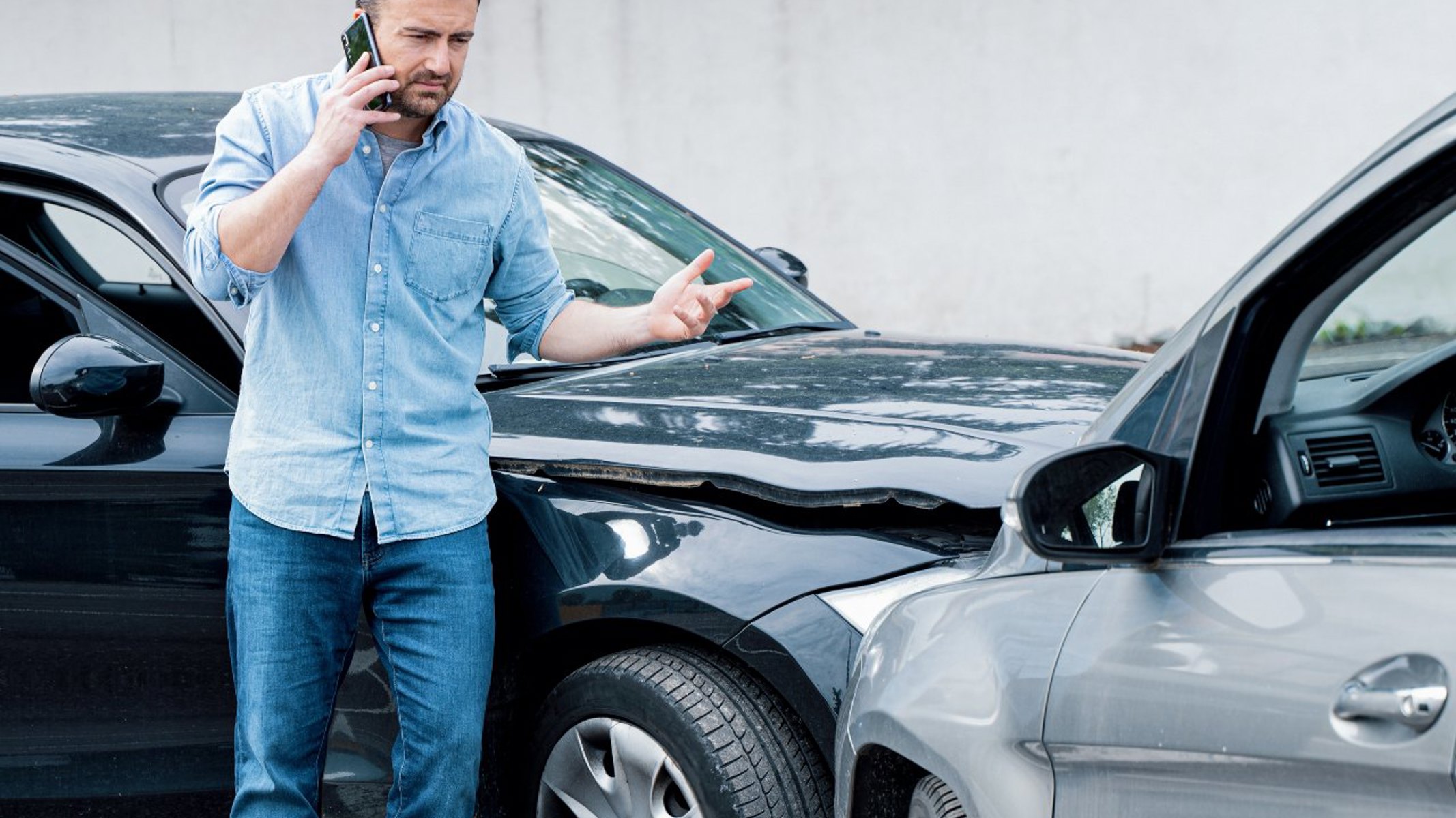 Frustreret mand taler i telefon ved siden af to biler, da han har lavet skade på en anden bil.
