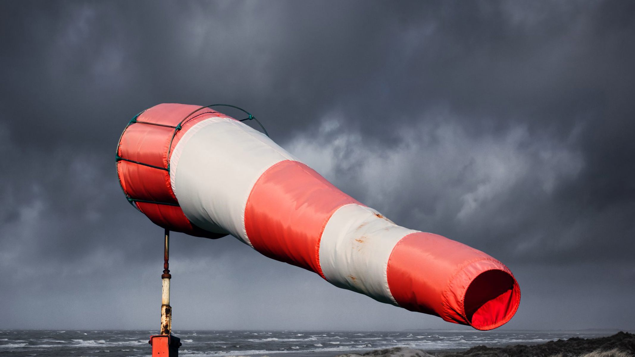 Rød og hvid vindpose på stranden, hvor der er sort himmel.