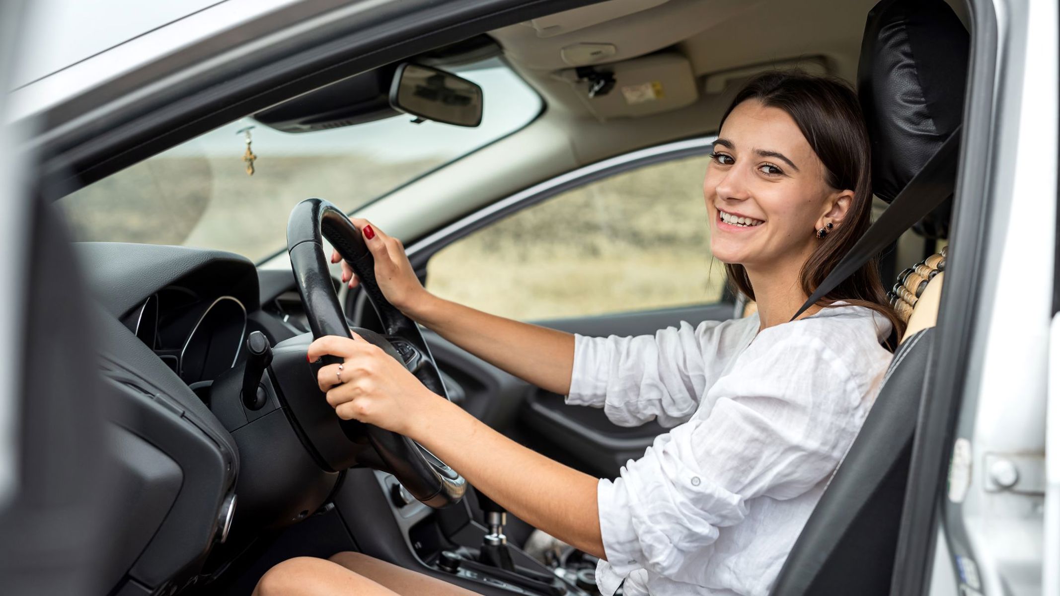 Ung pige sidder i bil med åben dør og smiler