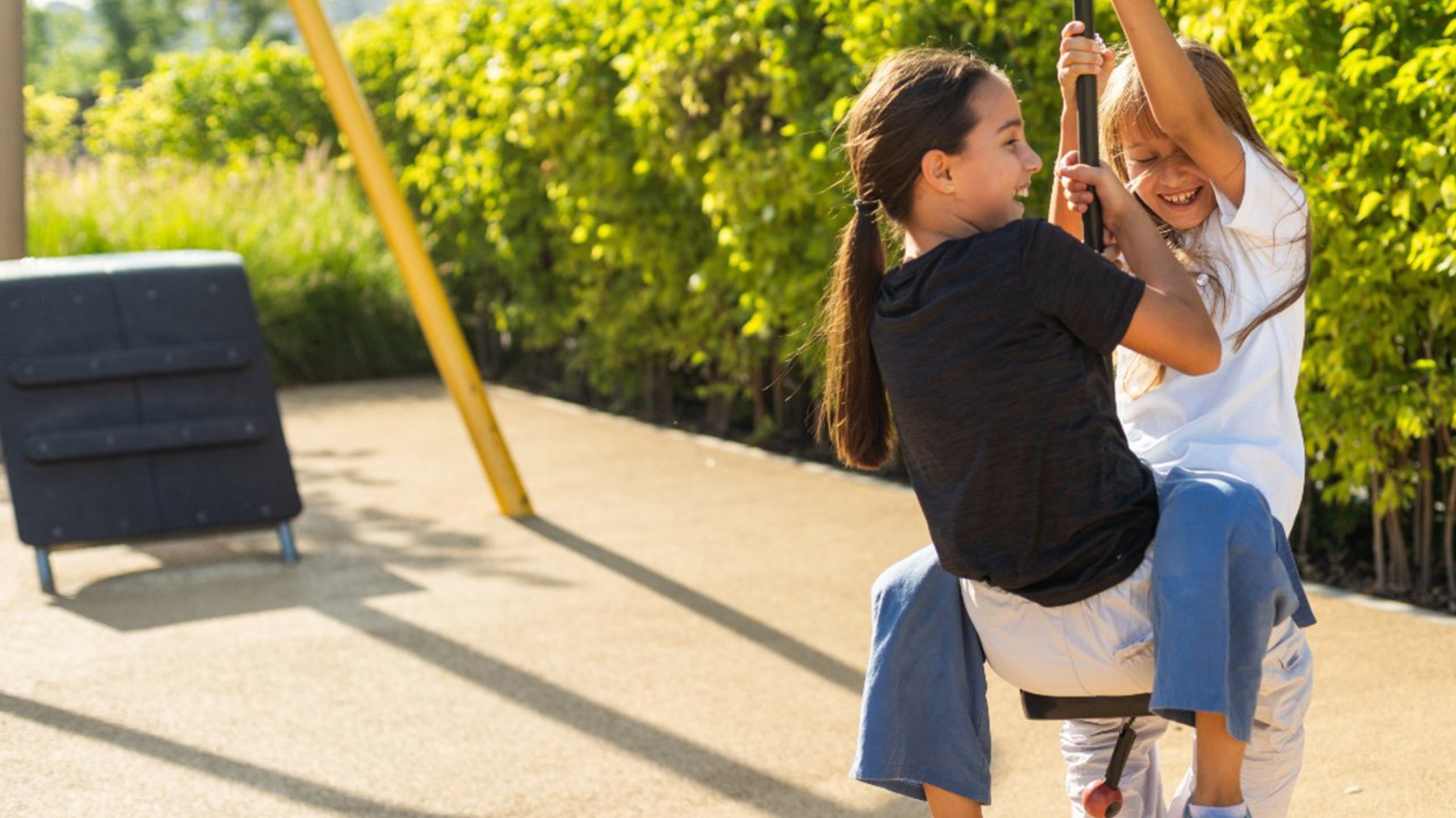 Billedet viser to glade skolebørn, der leger sammen på en legeplads. Desværre kan ulykker ske, selv når børn har det sjovt. Men en børneulykkesforsikring giver tryghed - både i skolegården og i fritiden.