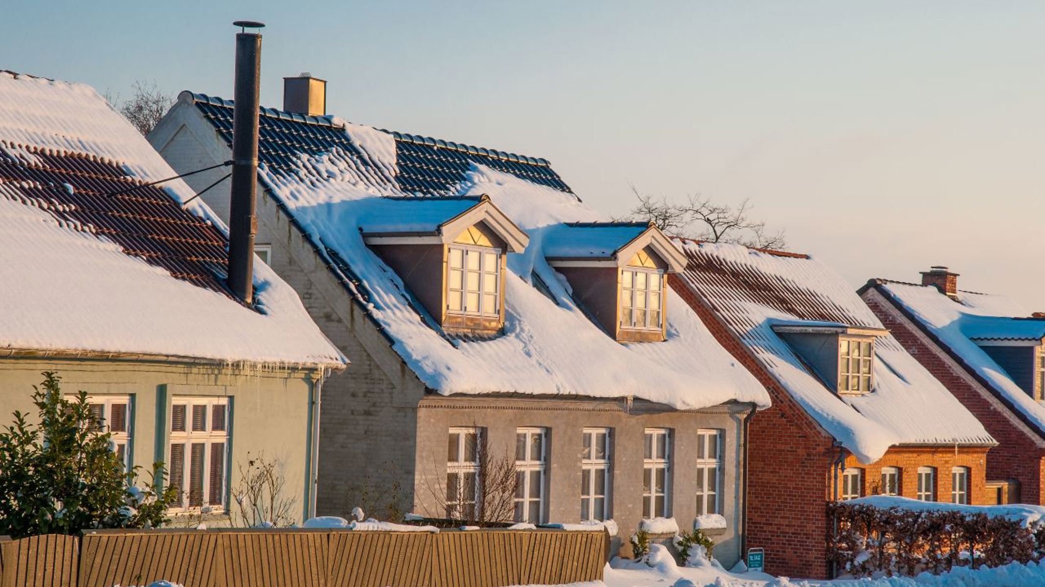 Fire huse på række med sne på tagene, og sne omkring.